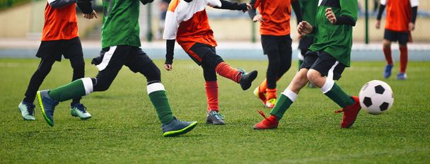 Ομάδα παιδιών που κλέβουν μπάλα ποδοσφαίρου. Παιδιά σε δύο ποδοσφαιρικές ομάδες τρέχουν πίσω από κλασική μπάλα ποδοσφαίρου. Οριζόντια αθλητικό υπόβαθρο. Πόδια των νέων παικτών στο γήπεδο ποδοσφαίρου - Φωτογραφία, εικόνα
