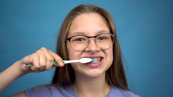 Κοπέλα με σιδεράκια βουρτσίζει τα δόντια της με οδοντόβουρτσα από κοντά. Ένα κορίτσι με χρωματιστά σιδεράκια στα δόντια της κρατάει τα δόντια της καθαρά.. - Φωτογραφία, εικόνα