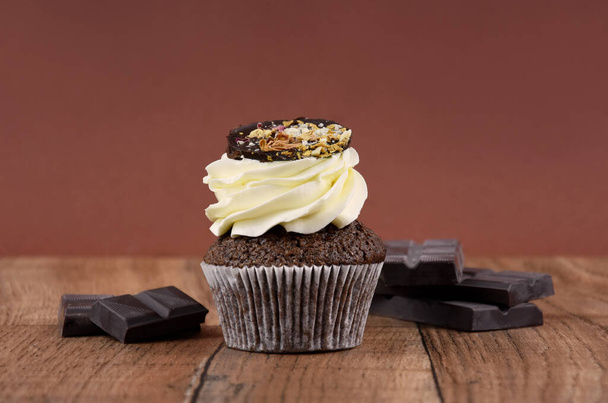 Chocolate cupcake with vanilla frosting on a wooden background stock images. Delicious cupcake with a pile of chocolate brown frame stock images. Chocolate cupcake brown border with copy space for text - Φωτογραφία, εικόνα