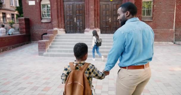 Οι πολυεθνικοί γονείς φέρνουν παιδιά στο σχολείο. Καυκάσια μαθήτρια τρέχει στο σχολείο. Αφρο-αμερικάνος πατέρας μιλάει με αγόρι κοντά στο σχολείο σε καλή διάθεση. Ο σχολιαρόπαιδο τρέχει στα μαθήματα. Έννοια μελέτης - Πλάνα, βίντεο