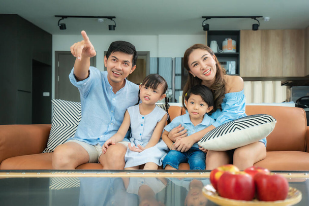 Asian happy family sitting and watching television in living room at home and spent quality time together for activity in vacation day, holiday, happiness or lifestyle concept - Photo, Image