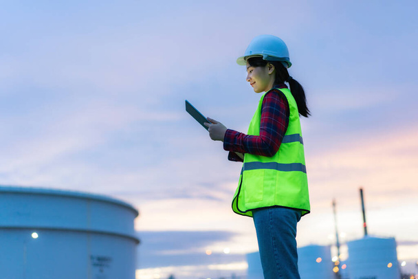 デジタルタブレットで夜間作業するアジアの女性石油化学エンジニア検査官の安全品質管理のために夜の石油・ガス精製プラント産業工場内 - 写真・画像