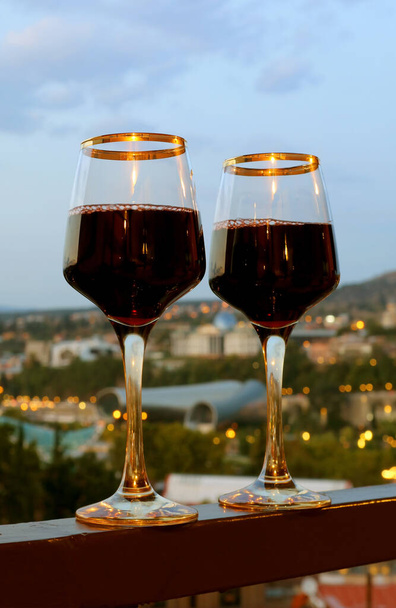 Par de copas de vino en el balcón con vista de noche borrosa de la ciudad en el telón de fondo - Foto, imagen