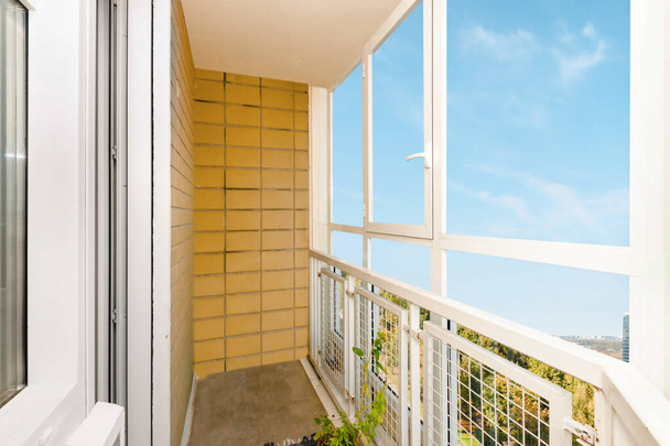 Большие чистые стеклянные раздвижные белые пластиковые окна балкона с горчично-желтой стеной и светло-голубой облачный вид на небо фон с копировальным местом. - Фото, изображение