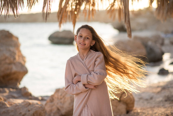 Beautiful long-haired girl on the beach. Girl in a beautiful dress near the sea. A child at sunset - Foto, Imagem