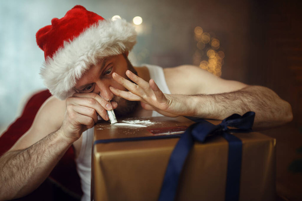 Slechte Kerstman neemt drugs, smerige cocaïne party, humor. Ongezonde levensstijl, man met baard in vakantiepak, nieuwjaar en alcoholisme - Foto, afbeelding