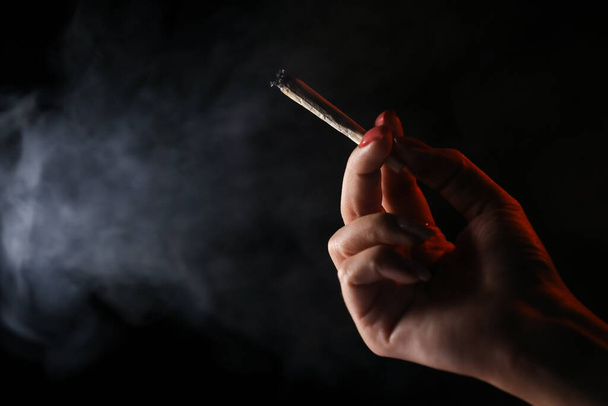 Donna mano tenuta sigaretta in un fumo su sfondo nero. Fumo cannabis. Uso medico.  - Foto, immagini