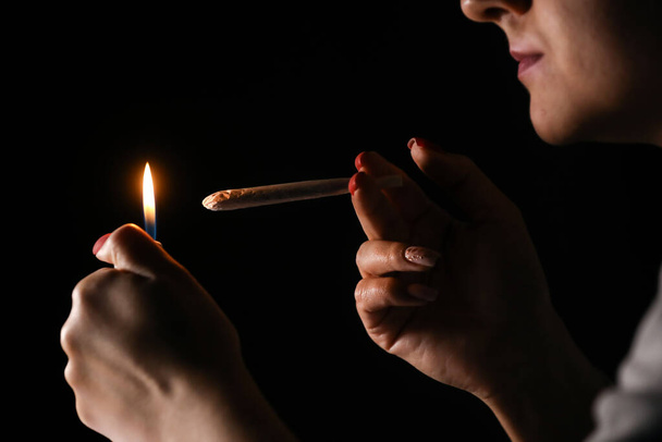 Woman hand holding cigarette in a smoke against black background. Smoking cannabis joint. Medical use. - Photo, Image