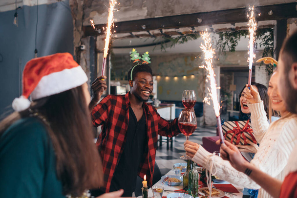 Group of people celebrating Christmas or New Year eve. Friends toasting drinks and enjoying dinner together. - Photo, Image