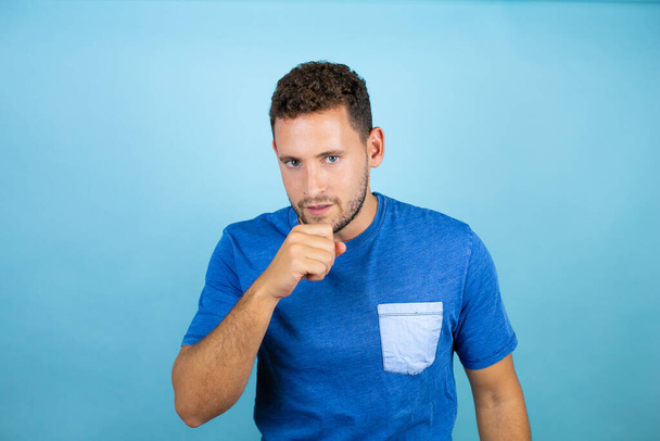 Fiatal jóképű férfi visel kék alkalmi póló felett elszigetelt kék háttér rossz közérzet és köhögés tüneteként hideg vagy hörghurut. Egészségügyi koncepció. - Fotó, kép