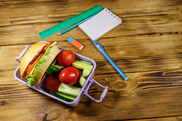 Back to school concept. School supplies and lunch box with burgers and fresh vegetables on a wooden table - Foto, immagini