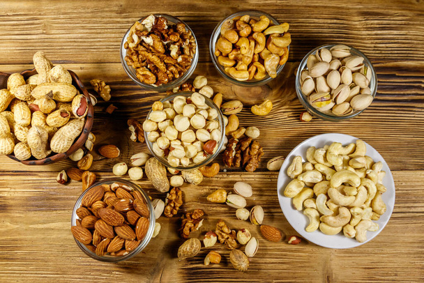 Assortiment van noten op houten tafel. Amandelen, hazelnoten, pistachenoten, pinda 's, walnoten en cashewnoten in kleine schaaltjes. Bovenaanzicht. Gezond eten concept - Foto, afbeelding