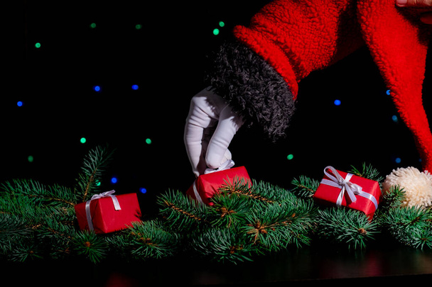 Рука Санта-Клауса держит красный подарок на черном фоне с рождественской елкой. - Фото, изображение