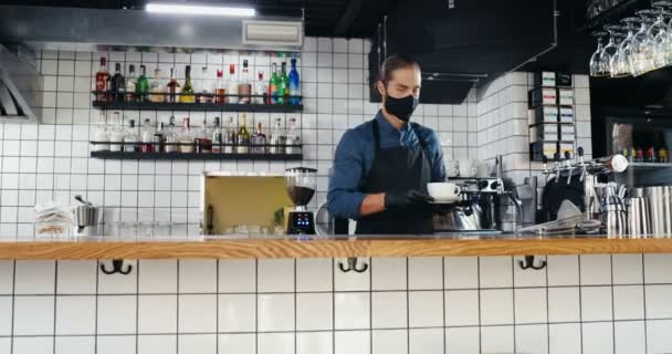 Portrait photo de jeune homme blanc beau barrista dans le masque et gants servant une tasse de café chaud sur le comptoir dans le café, en regardant la caméra. Serveur homme faire à boire et mettre sur le bar. Concept Covid-19 - Séquence, vidéo