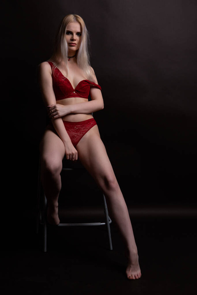 Сексуальна блондинка у червоній білизні Лейсі сидить на стільці на темному тлі. Фото зблизька. - Фото, зображення