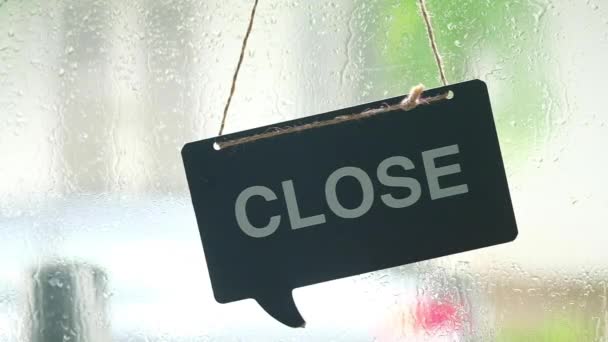 Hout opknoping teken van open op glazen deur tijdens stenen regen achtergrond - Video