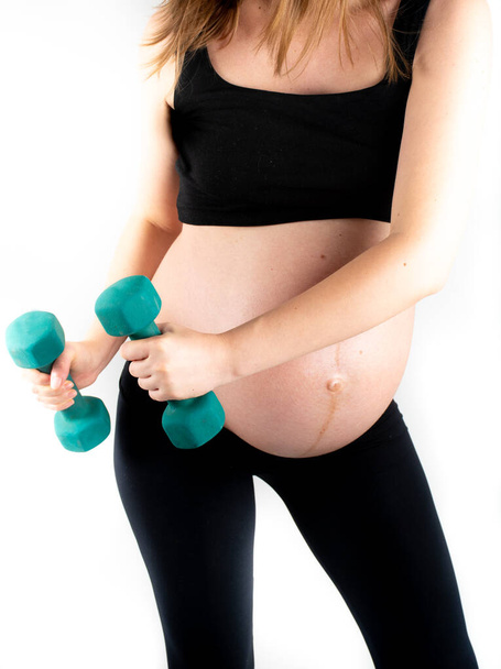 Active healthy pregnant woman exercising with dumbells, isolated on white background. The young expecting mother holding baby in pregnant belly. Maternity prenatal care and woman pregnancy concept. - Photo, Image