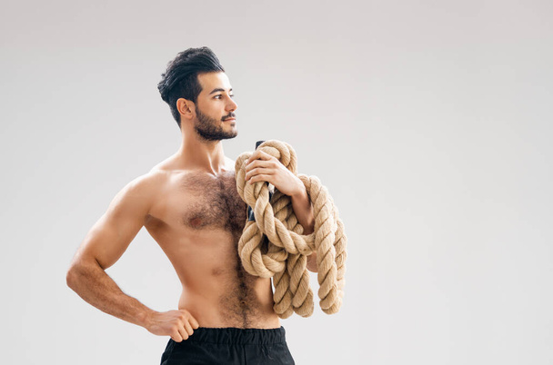 Athletic young man doing crossfit exercises with a rope on grey background.     - Φωτογραφία, εικόνα