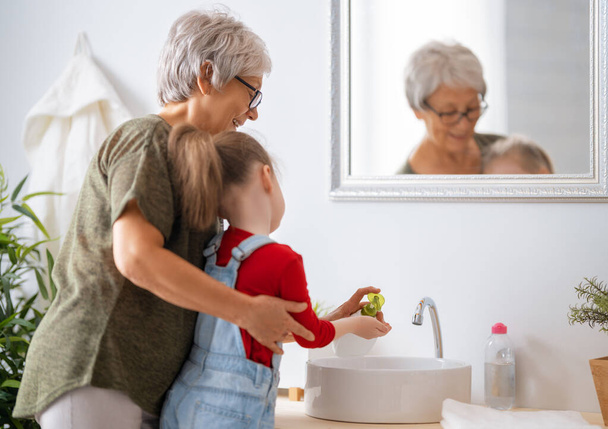 A cute little girl and her grandmother are washing their hands. Protection against infections and viruses.   - Zdjęcie, obraz
