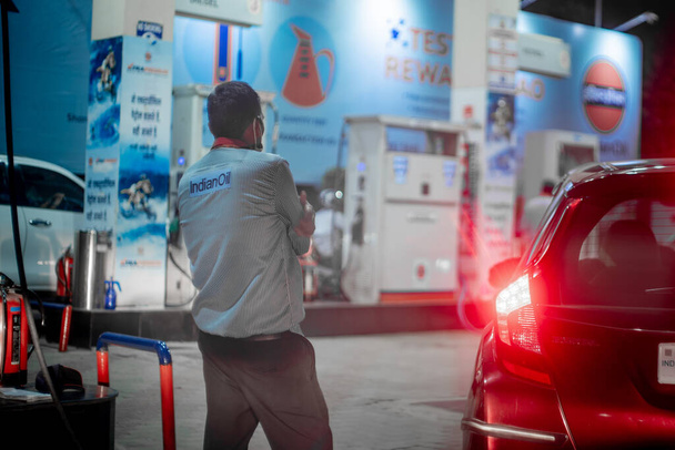 Pumpenjunge beim Tanken an einer indischen Zapfsäule in einem wartenden Auto mit Licht beim Schließen des Tankdeckels, während andere Autos einfahren, um Kraftstoff zu tanken - Foto, Bild