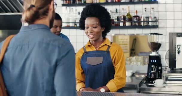 Pretty smiled African American female bartender serving and taking order from Caucasian guy. Rear of male client. Mixed-races. Customer buying coffee and talking with waitress in cafe. Multiethnic. - Footage, Video