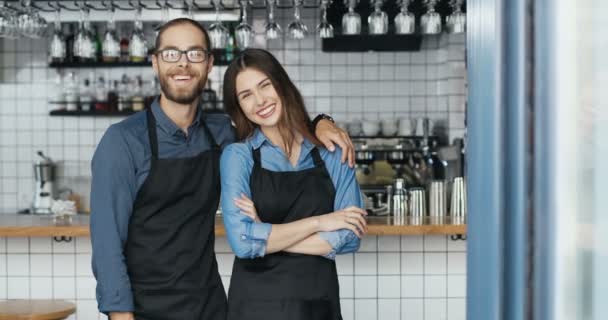 Portrait of Caucasian cheerful couple of bartenders in aprons hugging each other and smiling to camera happily. Happy waiter and waitress in hugs in cafe. Joyful man embracing woman. Baristas. - Footage, Video