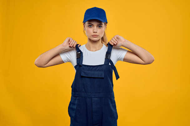 İş üniformalı kadın mavi şapkalı, kurye servisi sarı arka planda. - Fotoğraf, Görsel