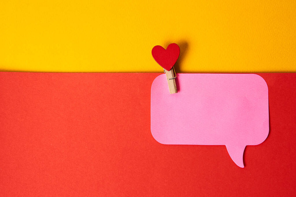 Coração vermelho em um clothespin e uma nota pegajosa rosa fundo colorido - Foto, Imagem
