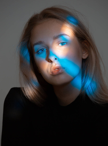 Fashionable beauty portrait of young girl posing in studio. Girl with blue light on her face - 写真・画像