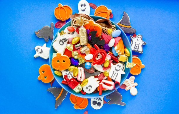 Halloween Jack o Lantern candy bowl with candy and halloween cookies Trick or Treat on blue background - Foto, immagini