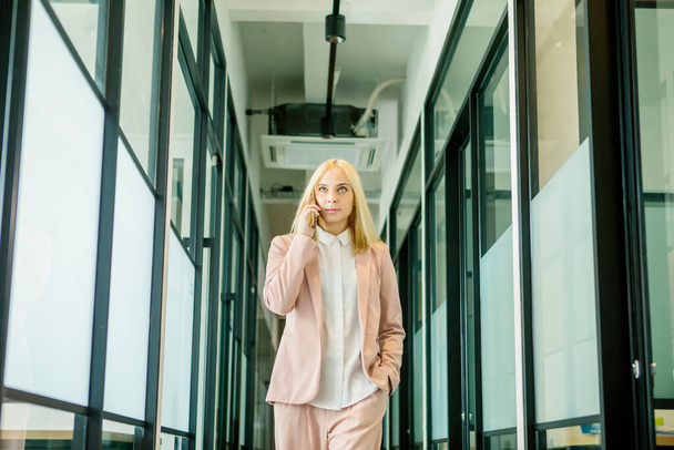 Blonde businesswoman makes a calling phone while standing in the office corridor - Foto, immagini