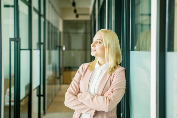 Close up of blonde businesswoman looks pensive while standing with folded hands in the office corridor - Fotografie, Obrázek