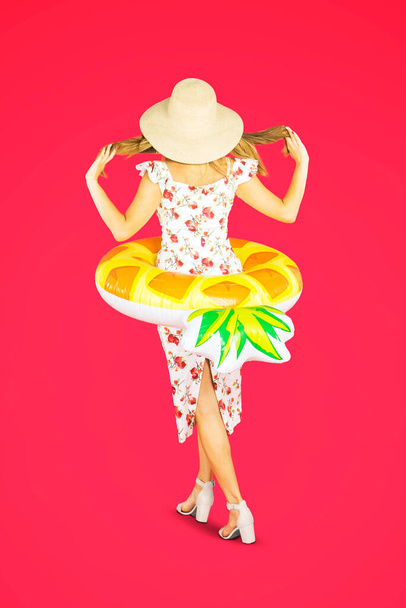 Rear view of young blonde woman walking with an inflatable float in the studio over red background - Foto, Imagem