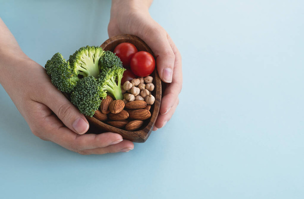 Aliments sains pour le cœur, concept de régime alimentaire. Les mains des femmes tiennent un bol avec des légumes, des amandes et des pois chiches sur fond bleu clair. Vue du dessus, espace de copie - Photo, image