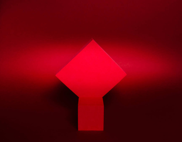 Foto van een helder podium (sokkel) van twee blokjes op een papieren achtergrond. In verzadigd rood, met gradiënt en graan. Reclame plaats. Blanco productstandaard en abstracte achtergrond met licht. - Foto, afbeelding