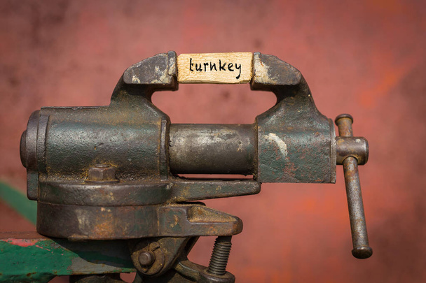 Vice grip tool squeezing a plank with the word turnkey - Photo, Image