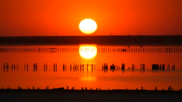 Incrível pôr do sol vermelho incrível com um enorme sol redondo em um lago de sal contra o pano de fundo de silhuetas de moinhos de vento - Filmagem, Vídeo