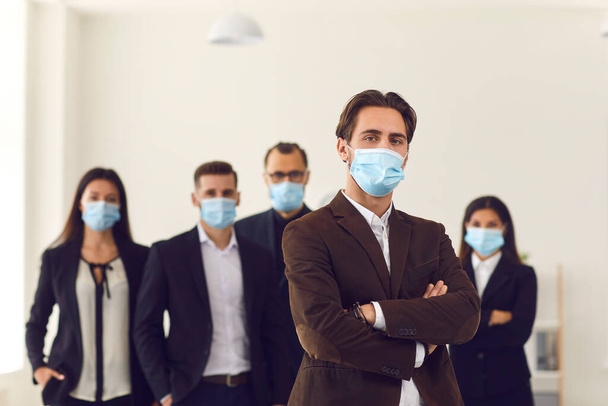 Male leader and team of responsible young company workers all wearing face masks at work - Фото, изображение