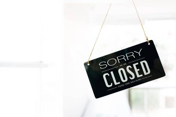 Sorry and Closed sign board through the glass of door in the cafe with clear interior white background and copy space. Cafe closed status during Covid-19 pandemic. Business service and food concept. - Photo, Image