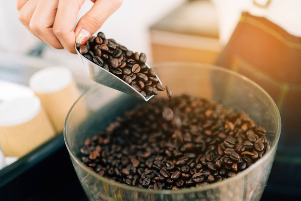 Sluit een vrouw schept koffiebonen in een elektrische koffiemolen. Koffieles voor startende ondernemers om een klein bedrijf te starten. - Foto, afbeelding