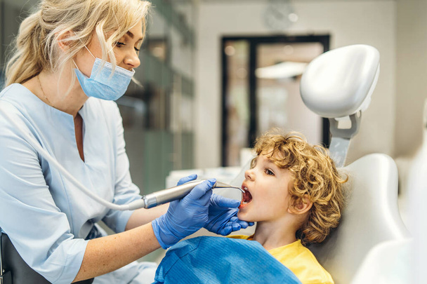 Cute young boy visiting dentist, having his teeth checked by female dentist in dental office - Foto, immagini