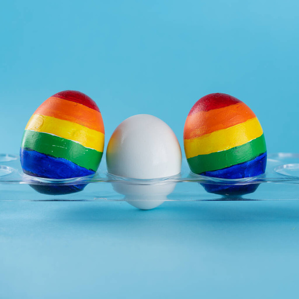 Rodzinę LBT. Jaja w kolorze flagi Igbt i białe jajo na niebieskim tle. Kreatywny pomysł na ilustrację prawa surogatów, prawo do adopcji par homoseksualnych i wychowania dziecka - Zdjęcie, obraz