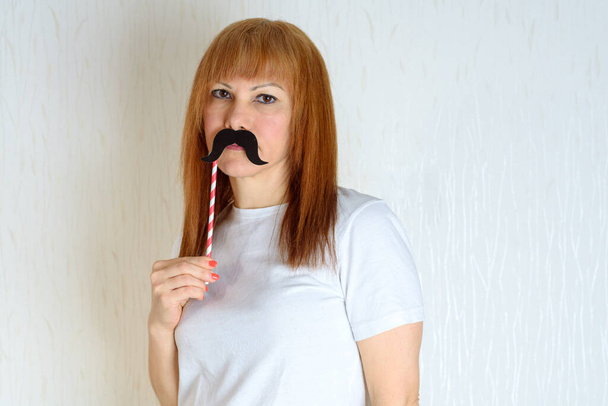 Attractive happy middle aged woman having fun with a fake moustache on stick. Senior female in period menopause. Lifestyle, Women's Health concept : playful mature ready for party. Impostor syndrome. - Photo, Image