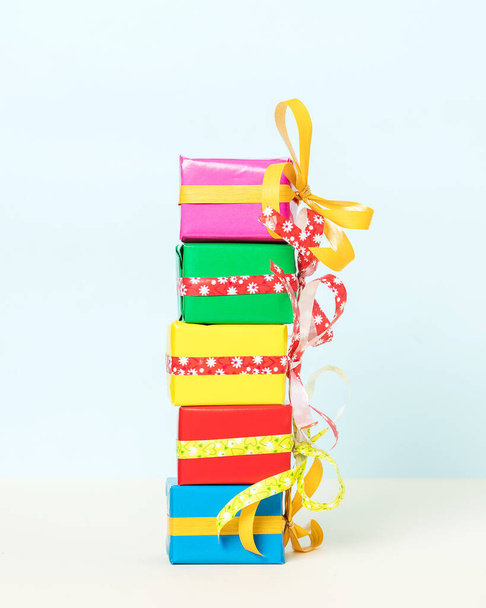 Πέντε πολύχρωμα κουτιά δώρων στοιβαγμένα σε παστέλ φόντο. Πρόσθια όψη. - Φωτογραφία, εικόνα
