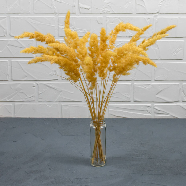 Un bouquet d'épillets secs dans un vase transparent en verre sur une table en béton sur un fond de brique blanche. Décor de maison élégant. Design d'intérieur moderne - Photo, image