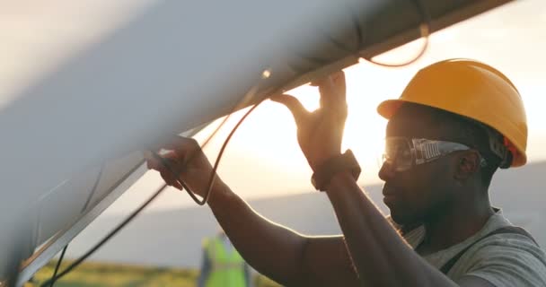 Close up of African American mechanic in protective helmet repairs solar panel with screwdriver. Technical review of modern technologies. - Footage, Video