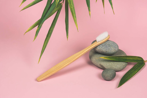 still life with bamboo toothbrushes, stones and bamboo leaves on a pink background - Fotó, kép