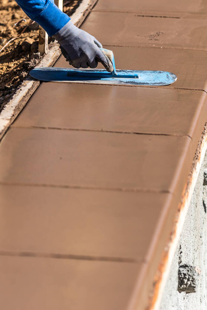 Trabalhador da construção civil usando espátula em cimento molhado formando enfrentamento em torno de nova piscina. - Foto, Imagem