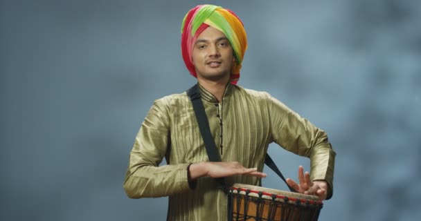 Retrato de músico indiano masculino em turbante tocando no tambor e sorrindo alegremente para a câmera. Homem bonito em roupa tradicional jogando no bongo com cara feliz. Músico com instrumento musical. - Filmagem, Vídeo