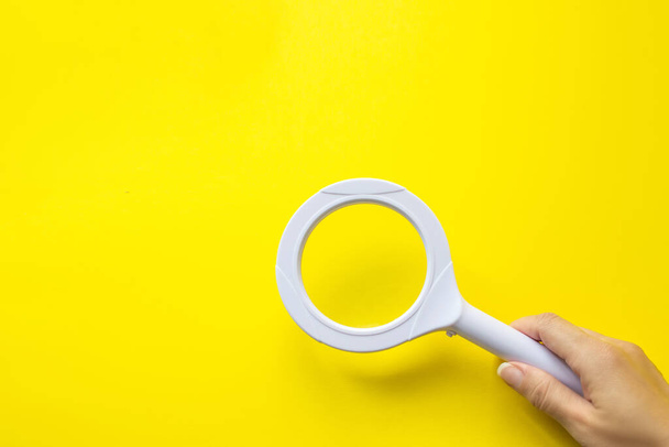 Close up hand holding magnifying glass on yellow background. SEO managment - Photo, Image
